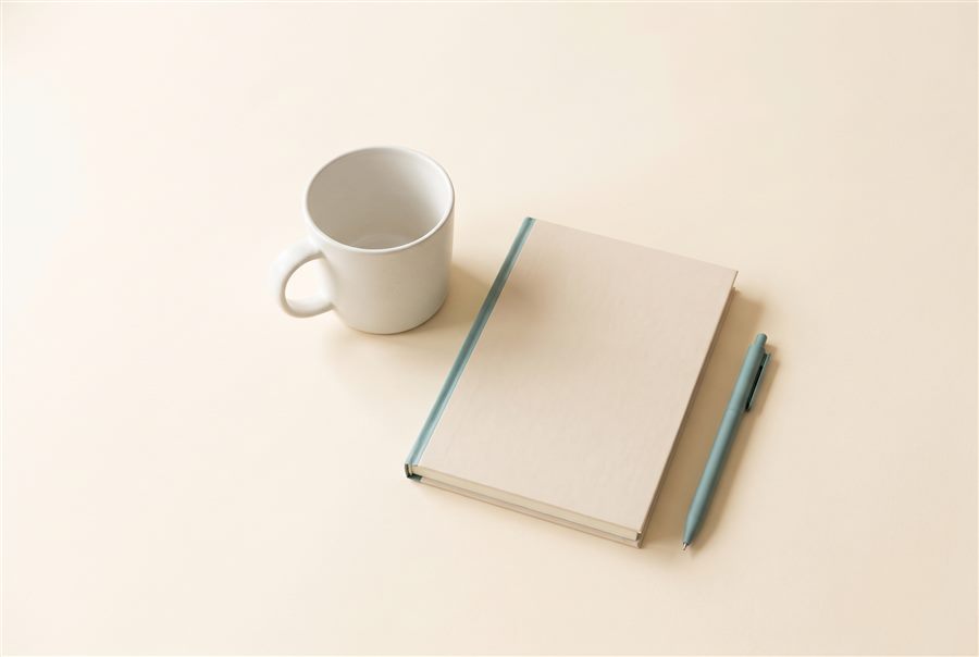 A notebook and pen beside a mug on a warm cream surface