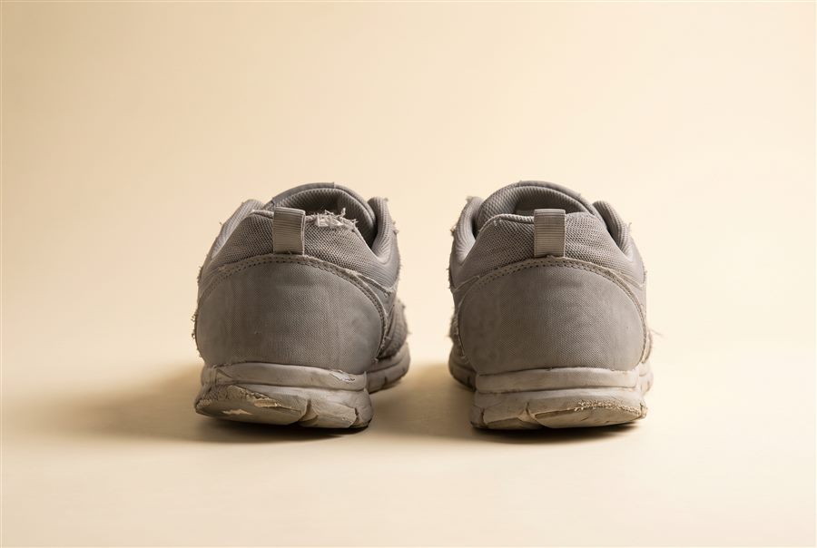 A worn pair of running shoes seen from behind, showing uneven heel wear