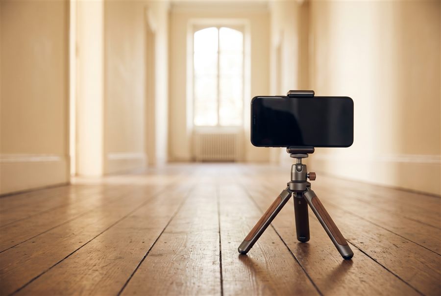A phone on a tripod set up to film someone walking down a hallway